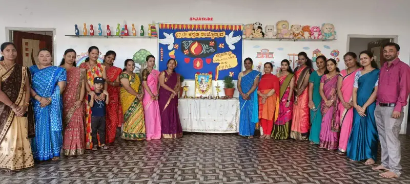 Adults and one child stand beside a decorated table and a SMARTKiDZ board with Kannada text and a lamp.