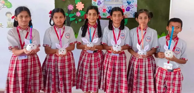 Six students in grey shirts and red checked uniforms hold small handmade rabbit models.